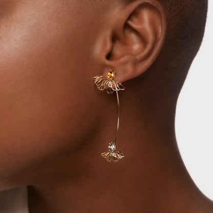 Gold earrings with a central gemstone worn by a person on a neutral background