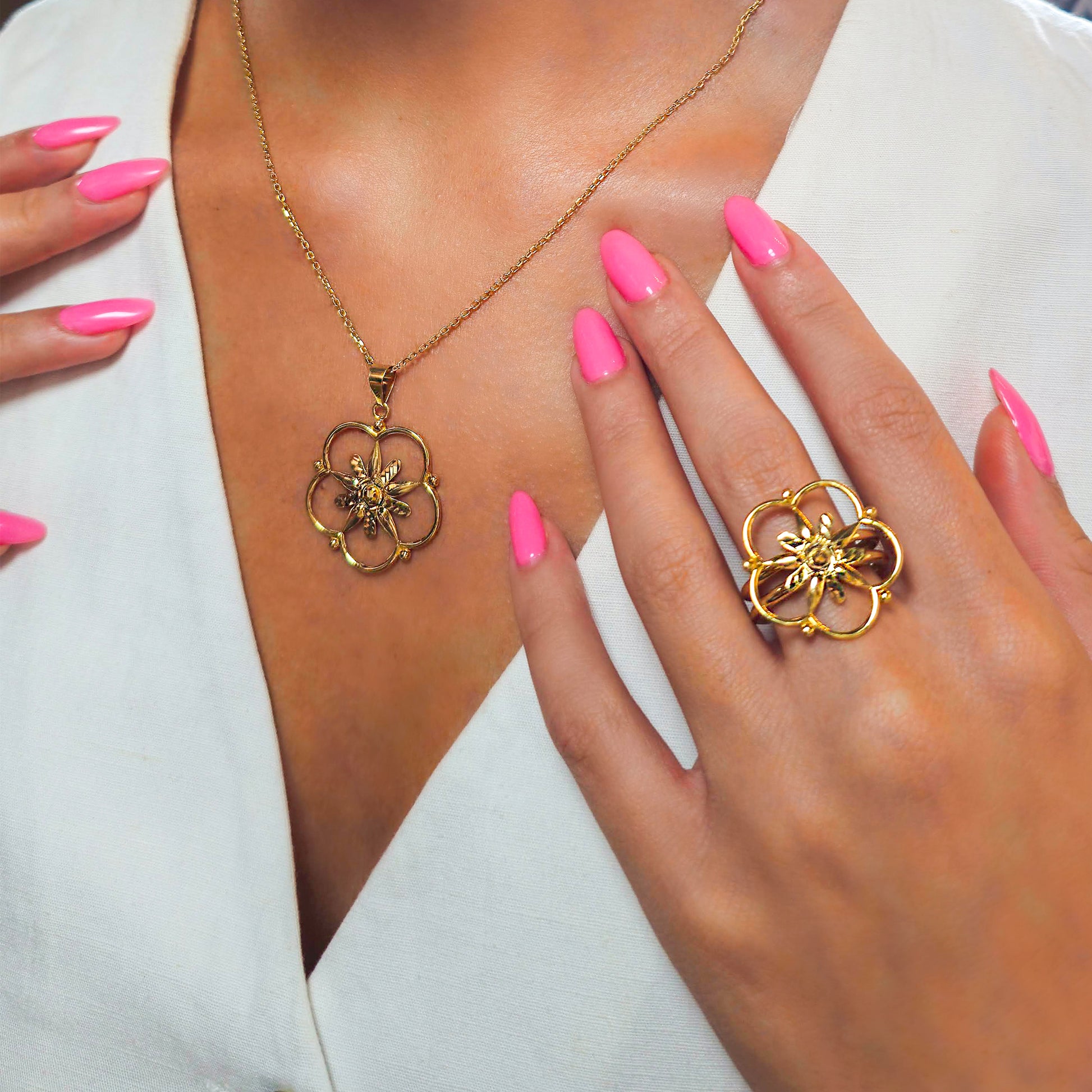 Gold necklace and ring with floral design worn by a person with pink nail polish.