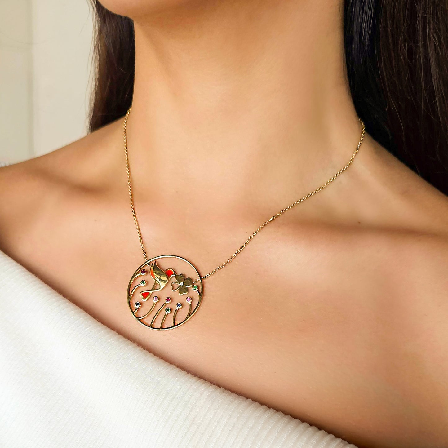 Gold necklace with a circular pendant on a person wearing a white sweater.