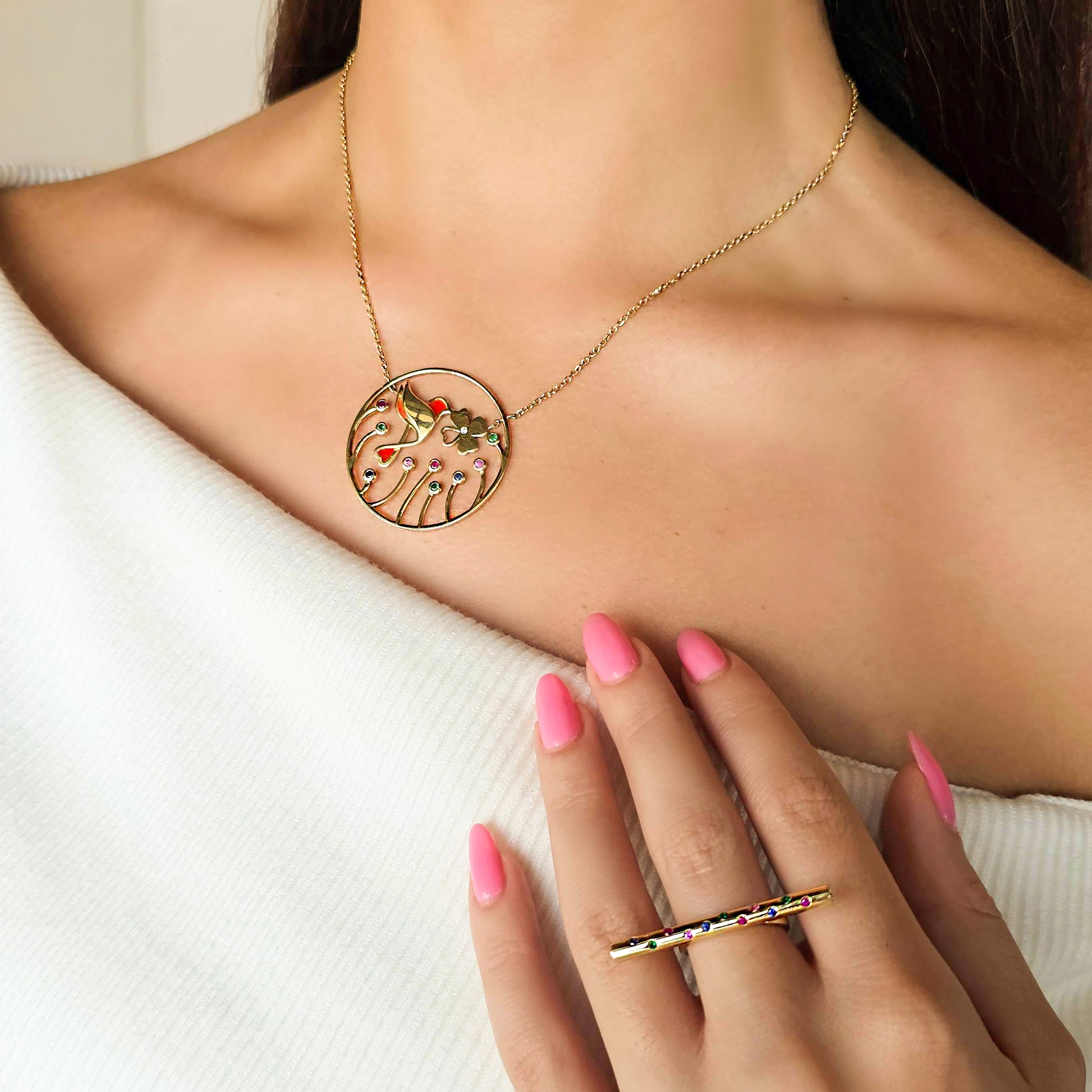 Gold necklace with a circular pendant worn by a person, with a hand also wearing a gold ring.