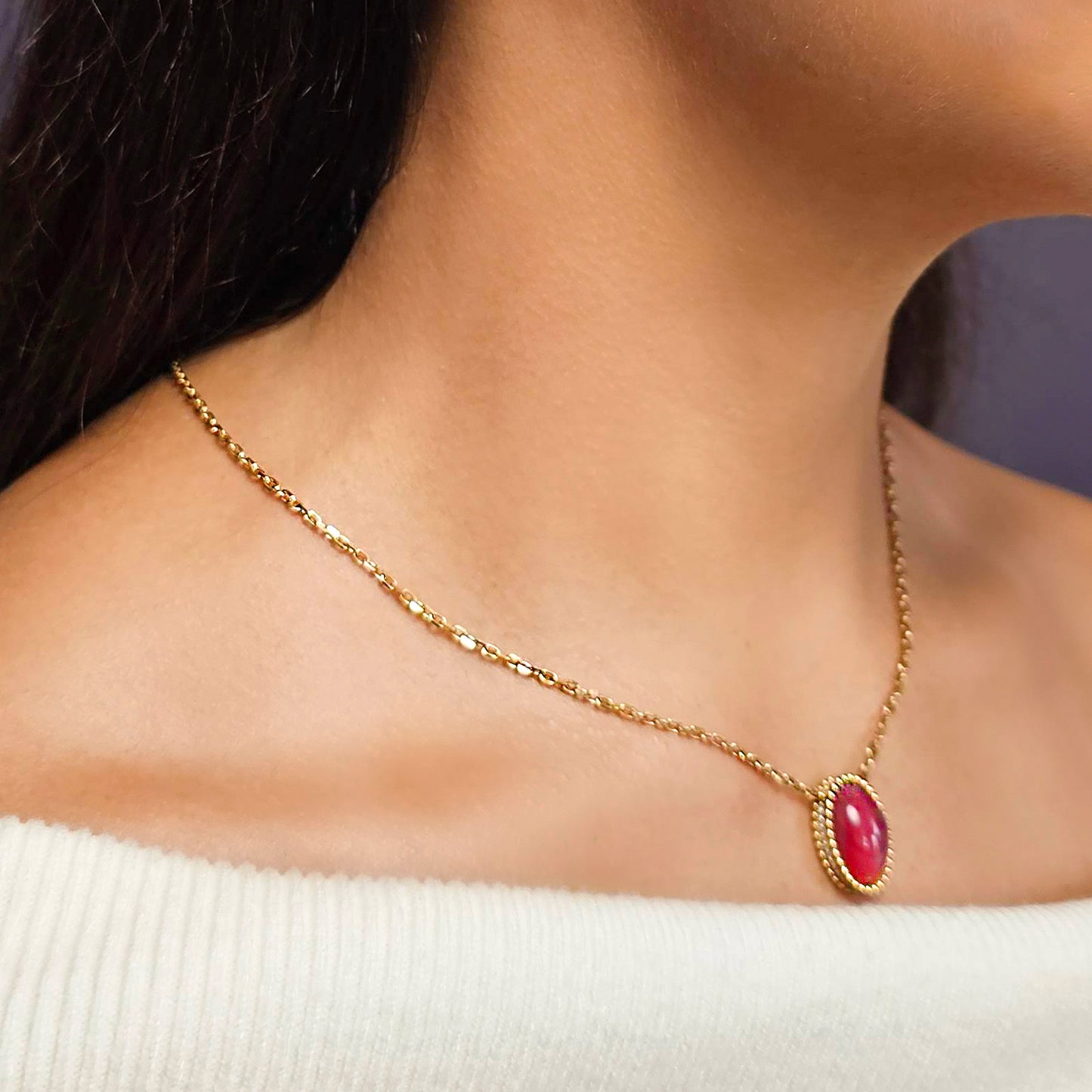 Gold necklace with a red gemstone on a person wearing a white sweater.