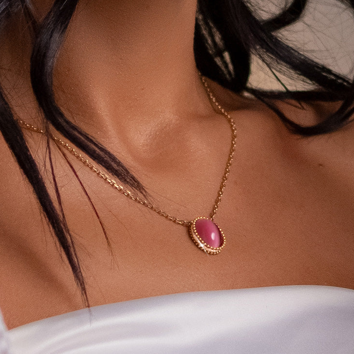 Necklace with a pink pendant worn by a person with white fabric in the background