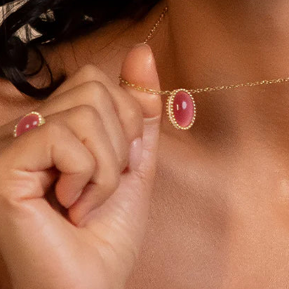 Close-up of a hand wearing a gold ring with a pink gemstone on a blurred background