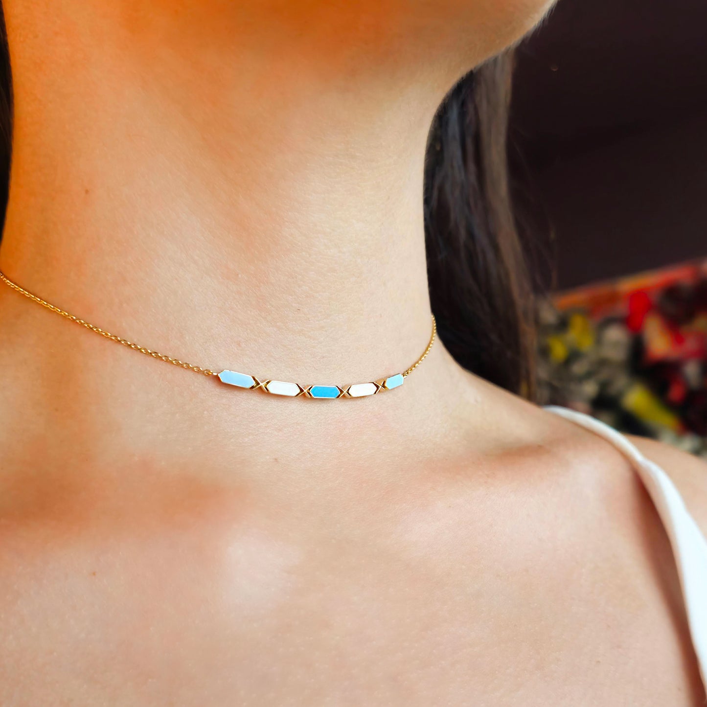Gold necklace with blue accents worn by a person, blurred background