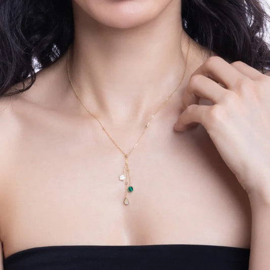 Woman wearing a delicate gold necklace with a green gemstone pendant.