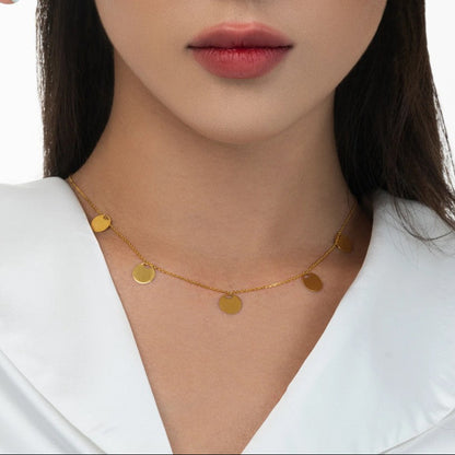 Gold necklace with round pendants worn by a person against a white background