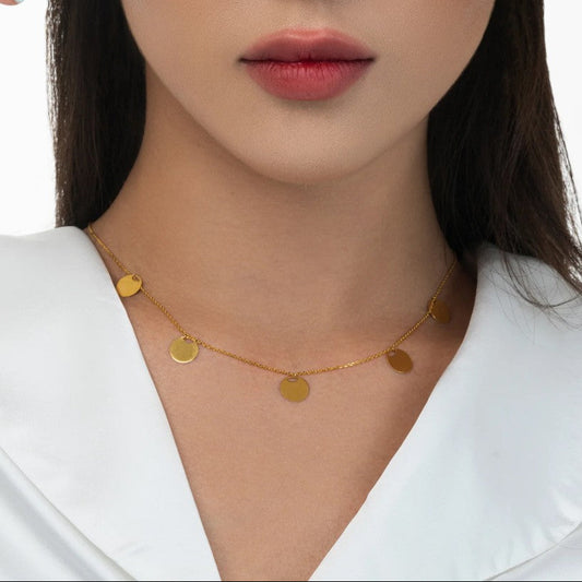 Gold necklace with round pendants worn by a person against a white background
