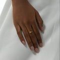 Hand wearing a gold bracelet and ring on a white fabric background