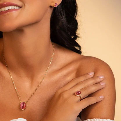 Woman wearing a gold necklace and ring with a pink gemstone on a beige background