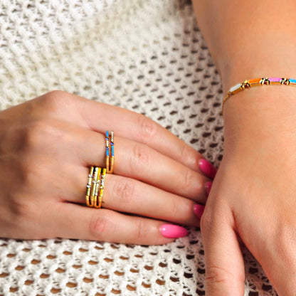 Close-up of hands wearing gold rings and a colorful bracelet on a textured fabric background