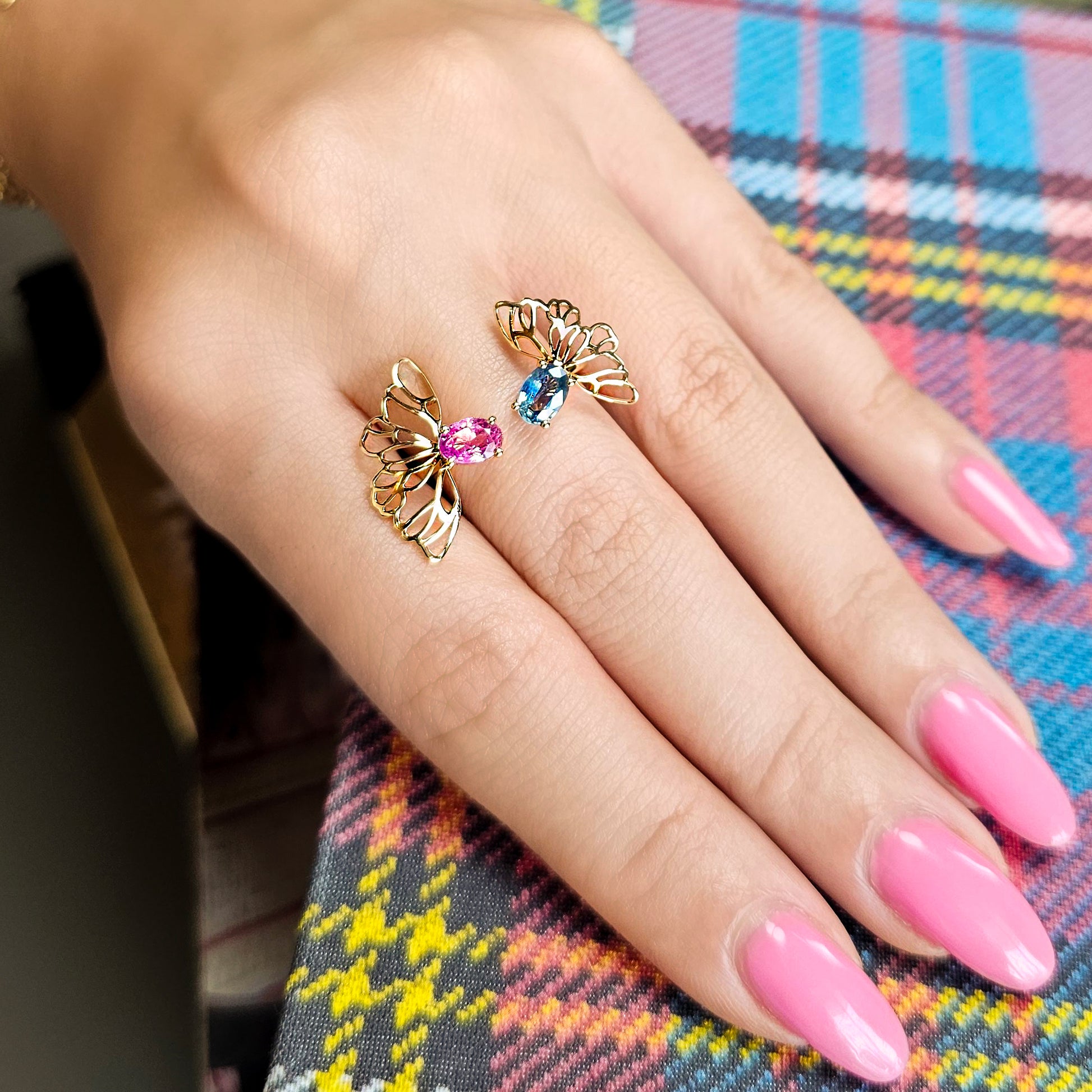 Hand wearing two gold butterfly rings with gemstones on a colorful plaid fabric background