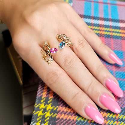 Hand wearing two gold butterfly rings with gemstones on a colorful plaid fabric background