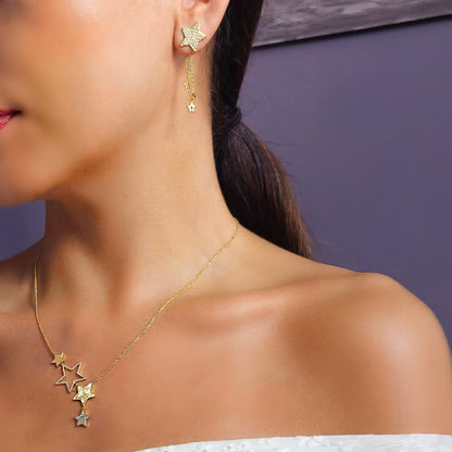 Close-up of a woman wearing gold star-shaped earrings and necklace against a purple background