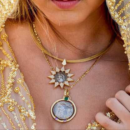 Close-up of a person wearing a gold necklace with a detailed pendant, set against a blurred background.