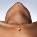 Gold necklace with a diamond pendant on a person's neck against a neutral background