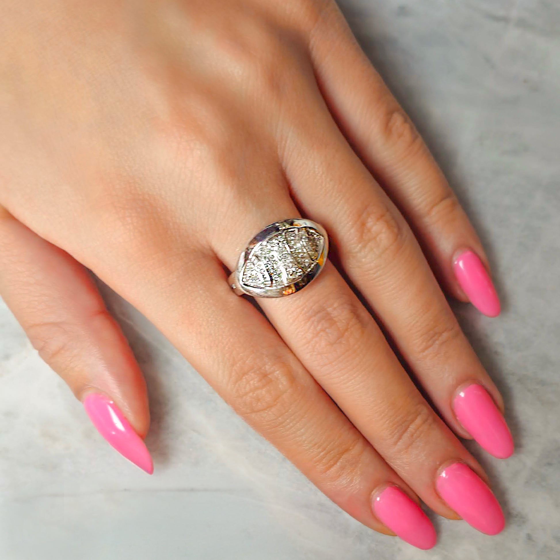 Hand wearing a large diamond ring with pink nail polish on a neutral background