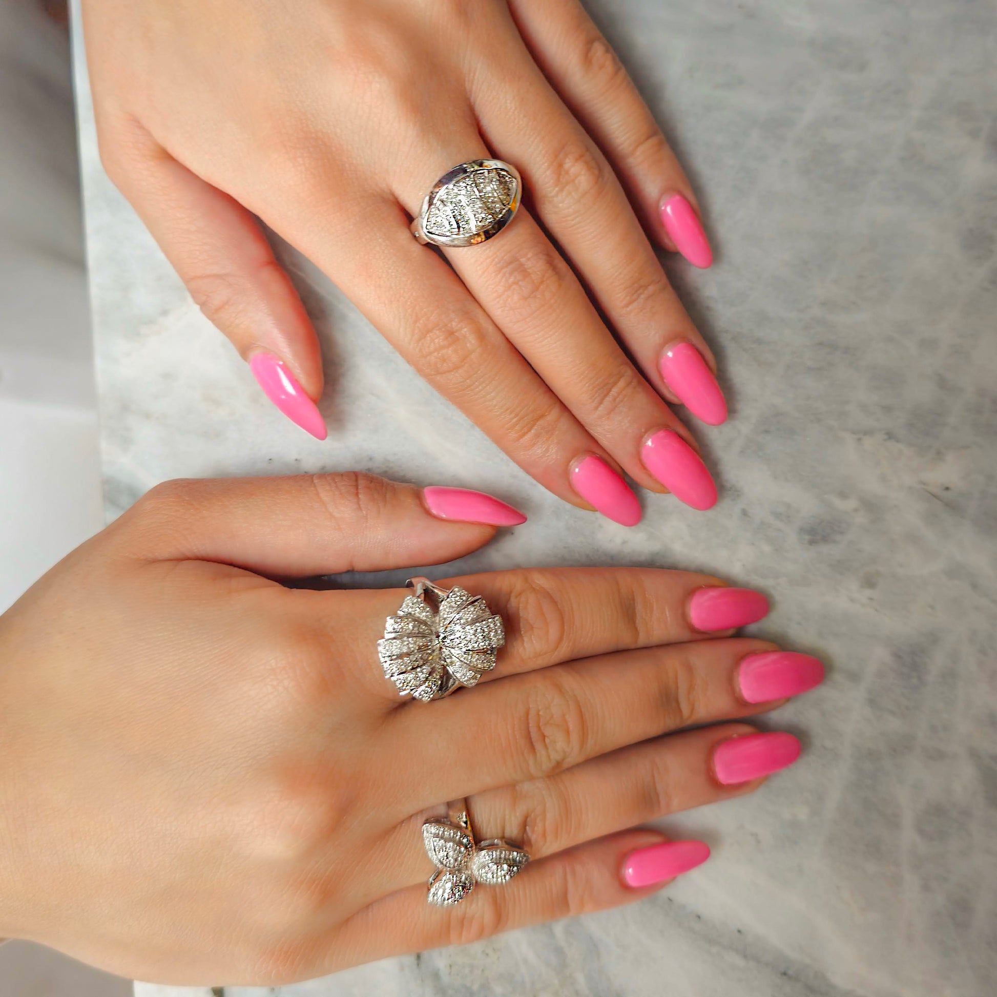 Close-up of hands with pink nails and gold rings on a marble surface