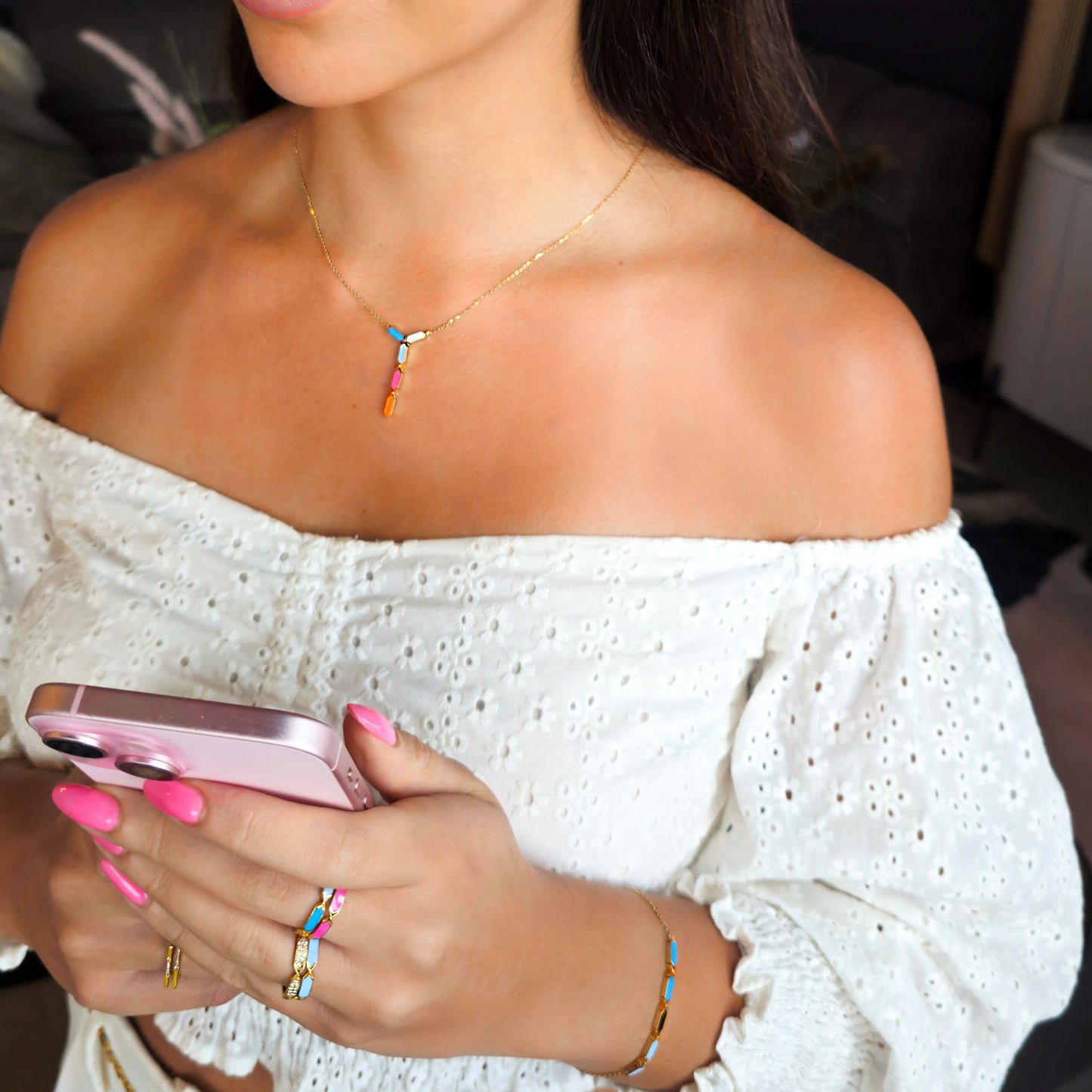 Woman holding a pink phone with colorful jewelry and a white off-shoulder top.