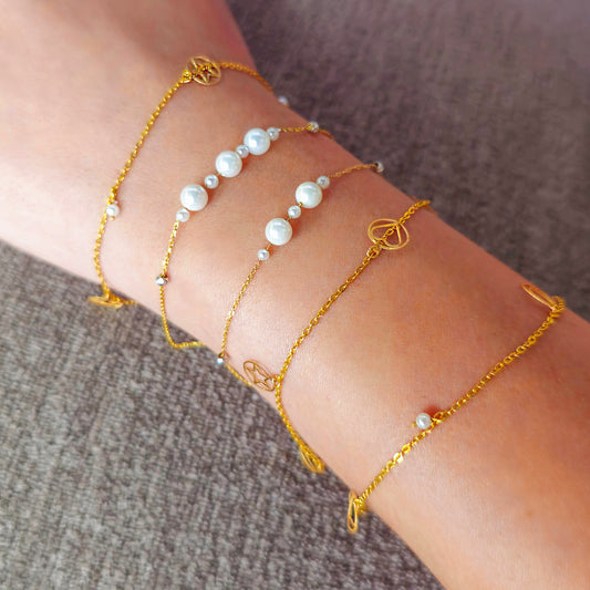 Gold bracelets with pearls on a wrist against a neutral background