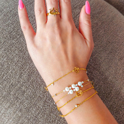 Hand wearing multiple gold bracelets and a ring on a textured surface