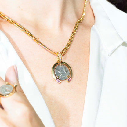 Gold necklace with a circular pendant worn by a person in a white outfit.