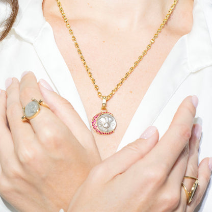 Person wearing gold jewelry including a necklace, ring, and bracelet on a plain background
