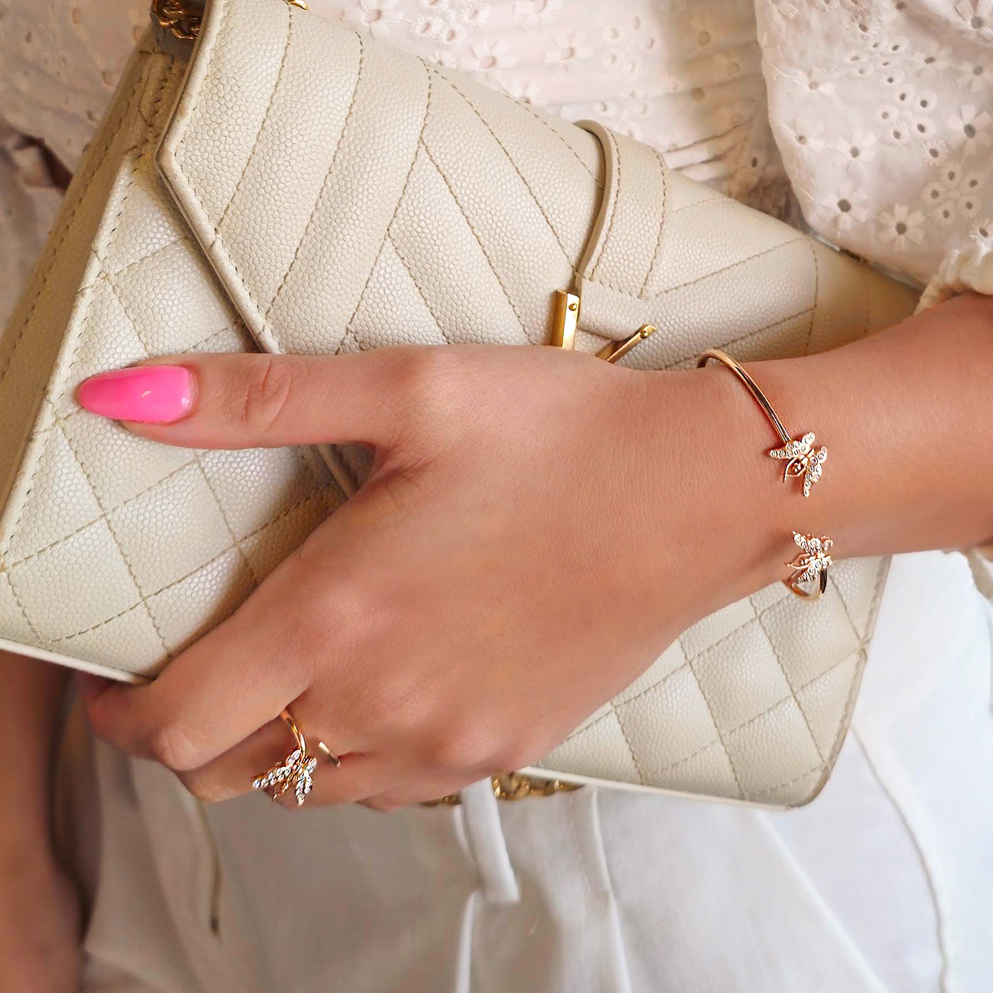 Close-up of a hand holding a beige quilted handbag with pink nail polish and gold jewelry.