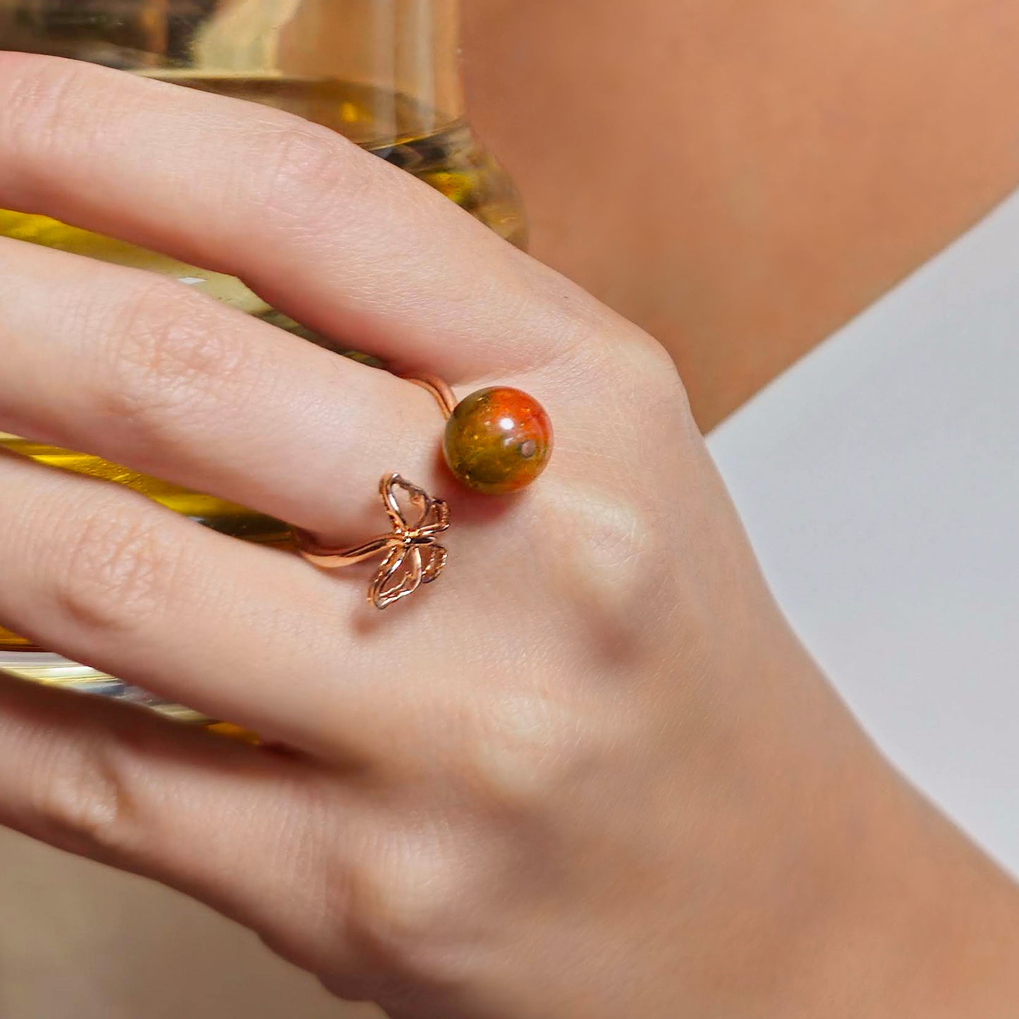 Hand wearing a ring with a red and orange stone, holding a glass of yellow liquid.