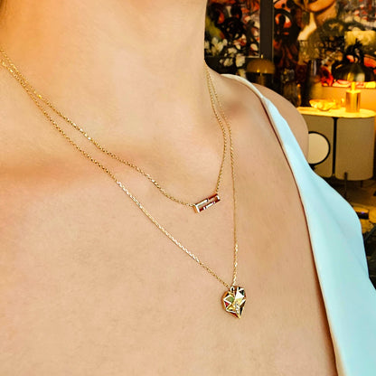 Gold necklace with a geometric pendant on a person wearing a light blue top, with a blurred background.