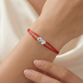 Red string bracelet with a diamond on a wrist against a neutral background