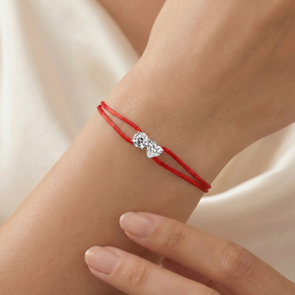 Red string bracelet with a diamond on a wrist against a neutral background