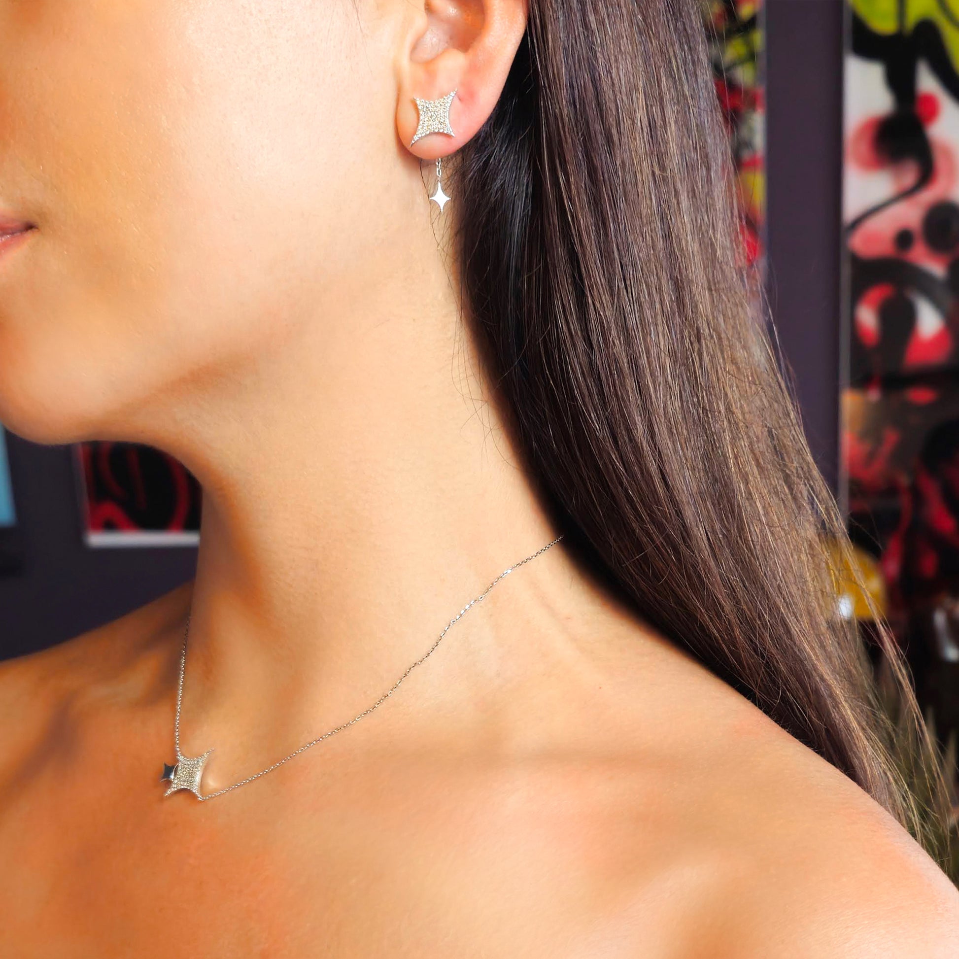 Close-up of a woman wearing diamond earrings and a necklace with a colorful abstract painting in the background.