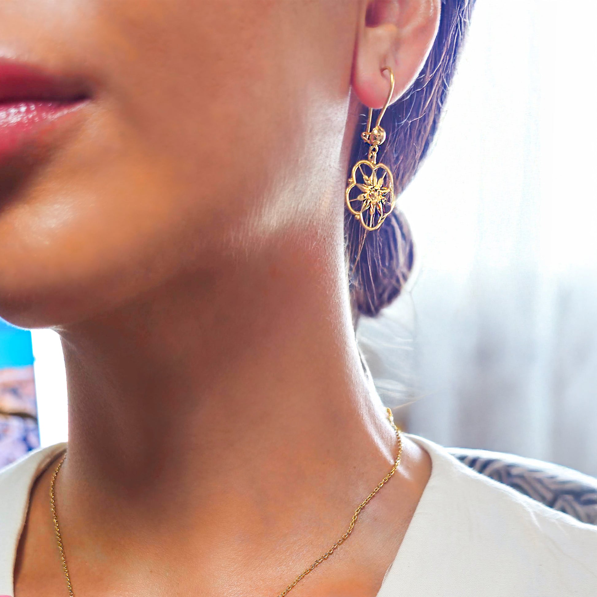 Close-up of a person wearing gold earrings and a necklace with a blurred background