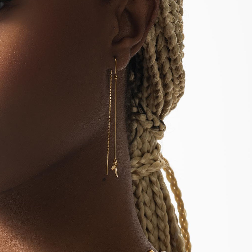 Gold threader earring worn by a person with braided hair on a neutral background