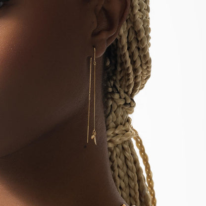 Gold threader earring worn by a person with braided hair on a neutral background