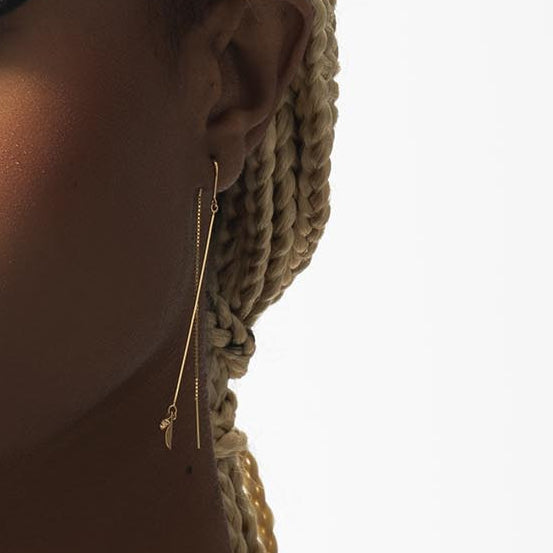 Gold earring worn by a person with braided hair on a white background