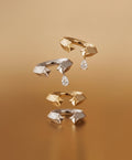Set of gold rings with geometric designs and diamond-like stones on a brown background