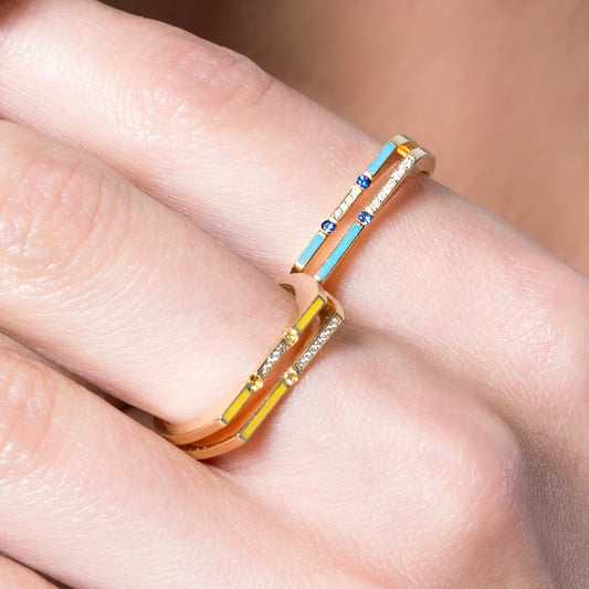 Gold ring with blue and yellow accents on a finger against a neutral background