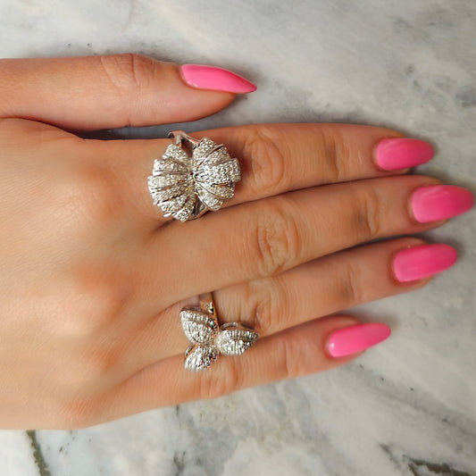 White gold butterfly rings on a hand with pink nail polish against a marble background