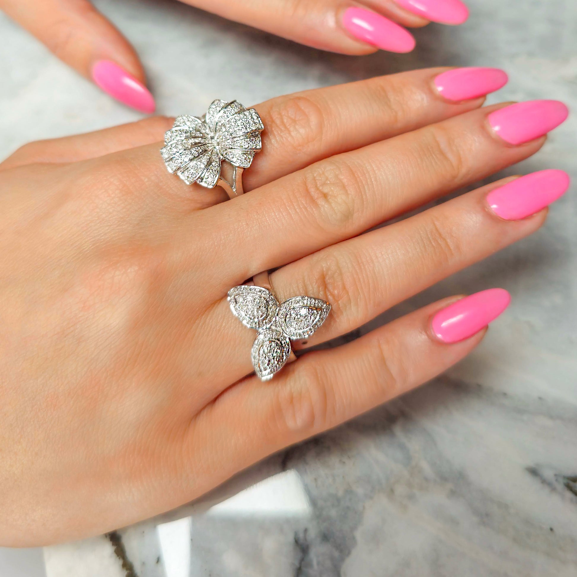 Gold butterfly rings on a hand with pink nail polish on a marble surface