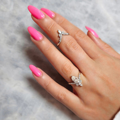 Hand with pink nails wearing two diamond rings on a gray background