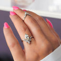 Hand wearing two white gold rings with gemstones against a blurred background