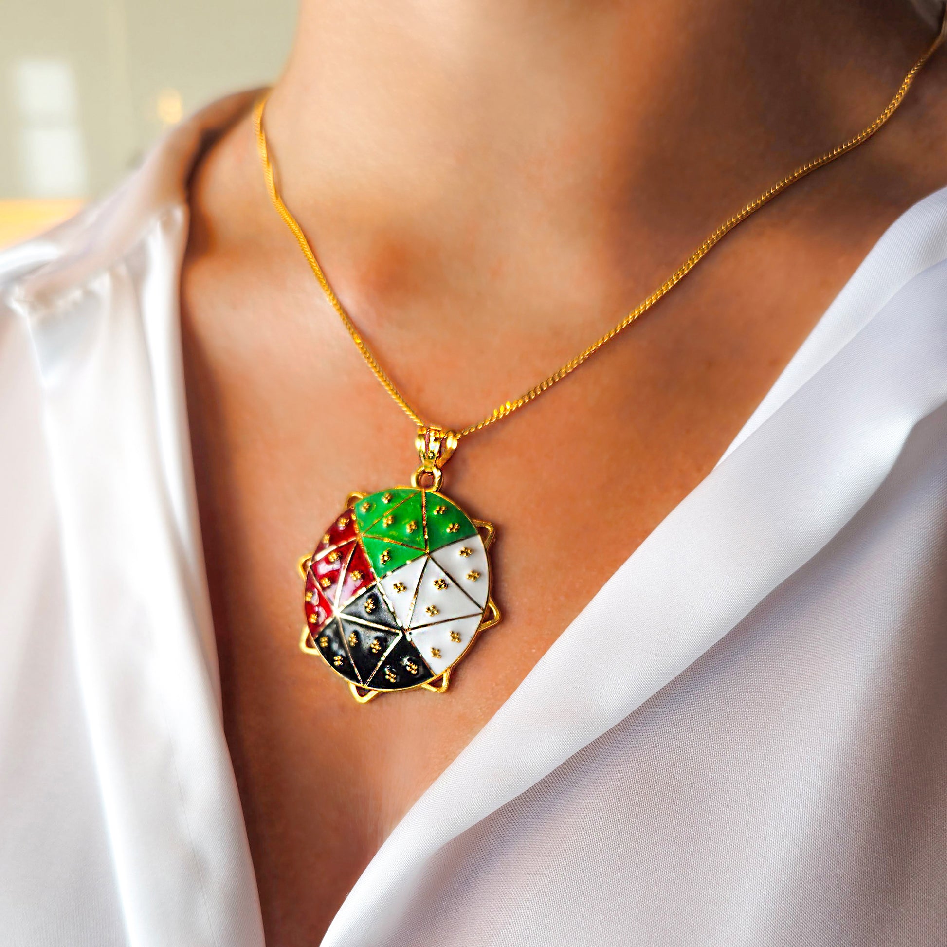 Gold necklace with a colorful pendant worn by a person in a white outfit.