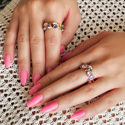 Close-up of two hands with pink nails and colorful rings on a textured fabric background
