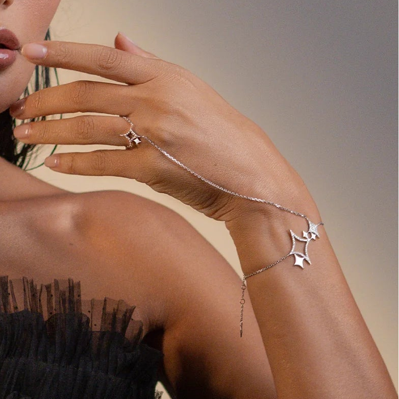 Close-up of a hand wearing a gold star-shaped ring and bracelet on a neutral background