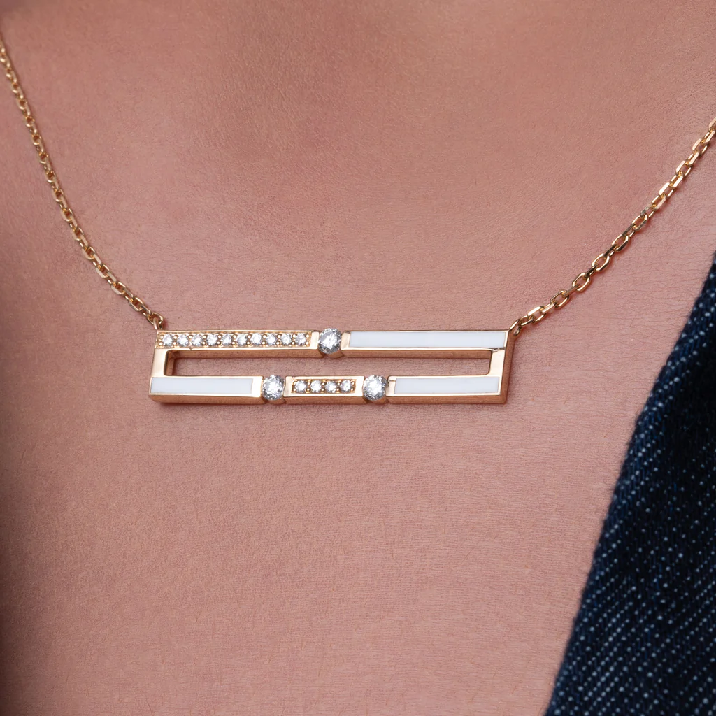 Gold necklace with a bar design featuring small diamonds on a person wearing a dark blue top.