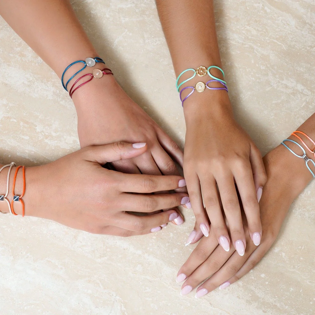 Three hands with colorful bracelets on a textured beige surface