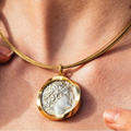 Gold necklace with a pendant featuring a classical design on a person's neck.