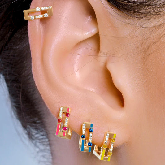 Close-up of an ear wearing gold earrings with colorful gemstones against a neutral background