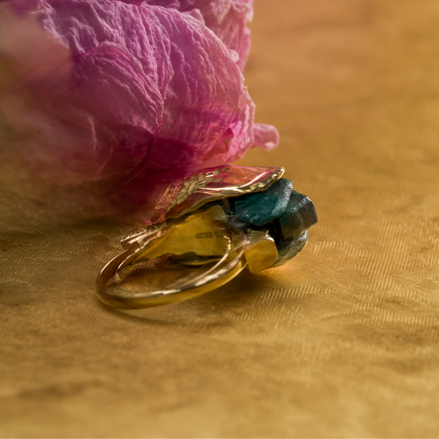 Gold ring with a green gemstone on a pink flower against a gold background